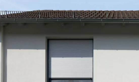 Ein Rolladen in einer hell angestrichenen Hausfassade schützt den Innenraum vor starker Sonne.