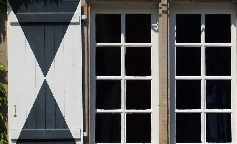 Fenster mit weiß-grau gemustertem Klappladen an der Seite.