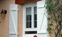 Weiße Klappläden an altmodischem Fenster mit bewachsener Hauswand.